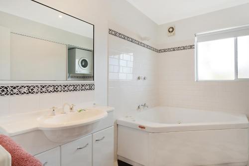 Baño blanco con lavabo, bañera y espejo en Beach Street Apartments, en Merimbula