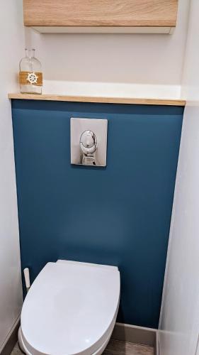La salle de bains est pourvue d'un mur bleu et de toilettes blanches. dans l'établissement Crevette rose à 100m de la plage de sable de Surtainville, à Surtainville