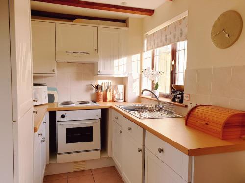 eine Küche mit weißen Schränken und einer Spüle und einem Herd in der Unterkunft Bay Tree Cottage - cosy home near beach in Woolacombe