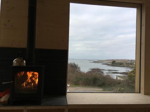 a fireplace in a room with a view of the water at Cala Fearnadh Off-Grid cabin, Bunessan, Mull in Bunessan