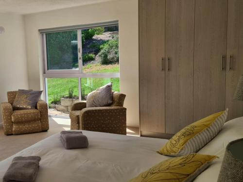 a bedroom with a bed and two chairs and a window at Southern Cross Beach House in Groot Brak Rivier
