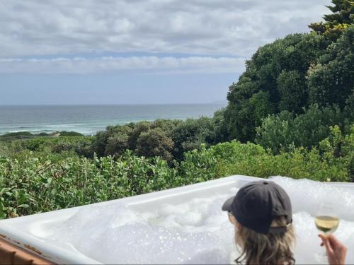 a person in a bath tub with a glass of wine at Southern Cross Beach House in Groot Brak Rivier