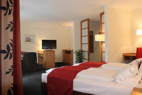 ein Hotelzimmer mit einem Bett und einem Flachbild-TV in der Unterkunft Ambassador Hotel in Grasbrunn