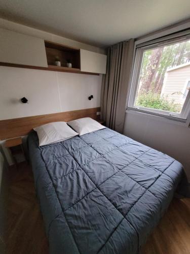 une chambre avec un lit avec une couette bleue et une fenêtre dans l'établissement MH 170 AVENTURA 3 chambres dont une suite parentale et 2 salles de bain dans camping 4étoiles, à Saint-Julien-en-Born