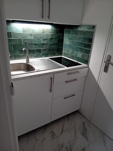una cocina con armarios blancos, fregadero y azulejos verdes en Chambre privée dans une maison individuelle, en Ronchin