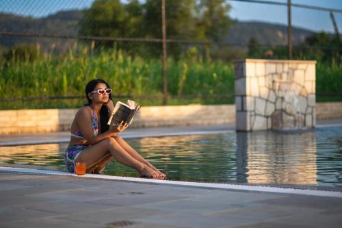 Eine Frau, die neben einem Pool sitzt und ein Buch liest. in der Unterkunft Aashiyana Luxury Cottages in Khilchīpur