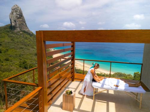 a woman sitting in a bed on a balcony with the ocean at Pousada Ecológica Akanã in Fernando de Noronha