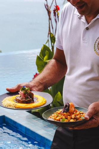 a man holding two plates of food on a table at Pousada Ecológica Akanã in Fernando de Noronha