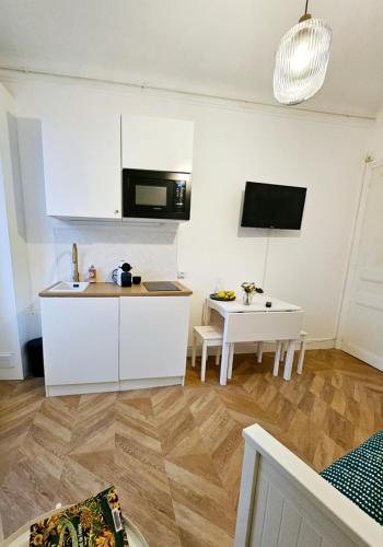 une cuisine avec des armoires blanches, une table et un micro-ondes dans l'établissement Studio Cœur de Deauville à 10 minutes à pied de la plage, à Deauville