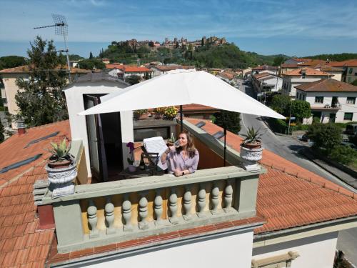a woman sitting on a balcony under an umbrella at La Torretta, Decameron View, sweet apartment in Certaldo