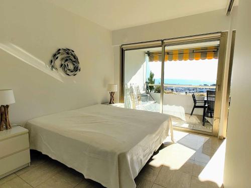 a white bedroom with a bed and a balcony at Appartement Moderne 4 Pers avec Clim et Parking, Villeneuve-Loubet Plage - FR-1-252A-36 in Villeneuve-Loubet