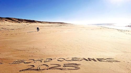 une personne debout sur une plage avec les mots et les océans écrits dans le sable dans l'établissement Les Bord'Océanes Sauna & Spa Villa Marensine et Villa Oyat, à Vielle-Saint-Girons