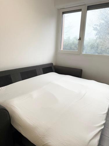 un lit blanc dans une chambre avec deux fenêtres dans l'établissement Studio Confort Pessac Centre avec Parking, à Pessac