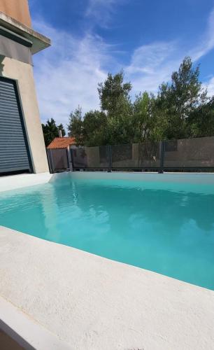une piscine avec de l'eau bleue devant une maison dans l'établissement Villa Camarguaise entre Plage et centre ville avec bassin extérieur, au Grau-du-Roi
