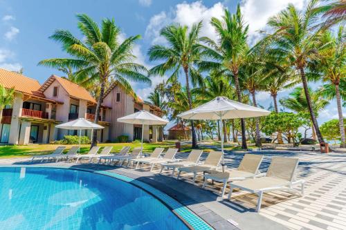 a pool with chairs and umbrellas and palm trees at Crystals Beach Resort Belle Mare, a member of Radisson Individuals in Belle Mare