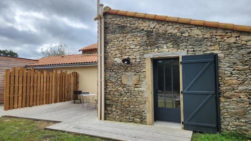 a stone building with a door and a wooden deck at Studio 2-3 pers in La Gaubretière