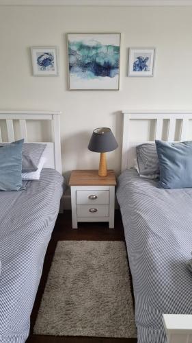 a bedroom with two beds and a lamp on a night stand at Cosy Bournemouth Bungalow in Longham