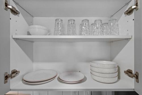 a white cabinet with plates and glasses on a shelf at Modern Apt W Pool, Gym & Free "p"prime Location in Rogers