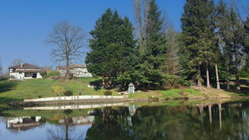 a lake with trees and a house in the background at Maison de l'olivier in Champniers-et-Reilhac