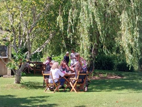 a group of people sitting at a table under a tree at Patons Rock Beach Villas in Takaka