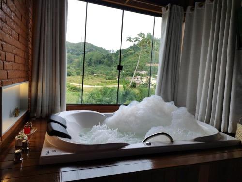 a bath tub filled with foam in a bathroom with a window at Domus Fiorese Chalés in Venda Nova do Imigrante