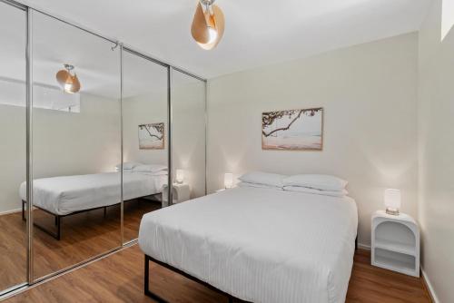 a white bedroom with a bed and a mirror at Stylish North Melbourne Stay, Minutes to CBD in Melbourne