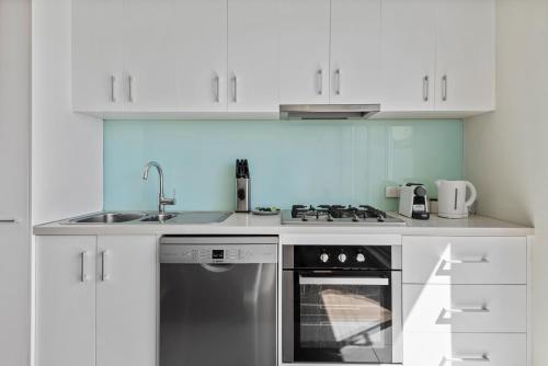 a white kitchen with a stove and a sink at Stylish North Melbourne Stay, Minutes to CBD in Melbourne