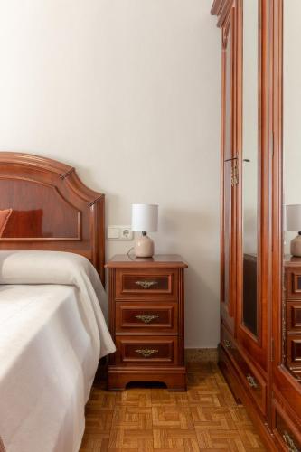 a bedroom with a bed and a dresser with a lamp at Apartamentos Asturias Holidays by Gestión House in Noreña