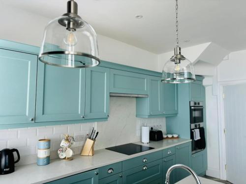 a blue kitchen with blue cabinets and three lights at Seascape Luxury sea front apartment in Bangor