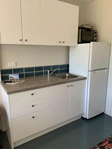 a white kitchen with a sink and a refrigerator at Private Olive Grove Studio in Mangonui