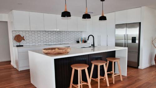 a kitchen with white cabinets and a counter with stools at The Pool House - Light and Spacious in Wamberal