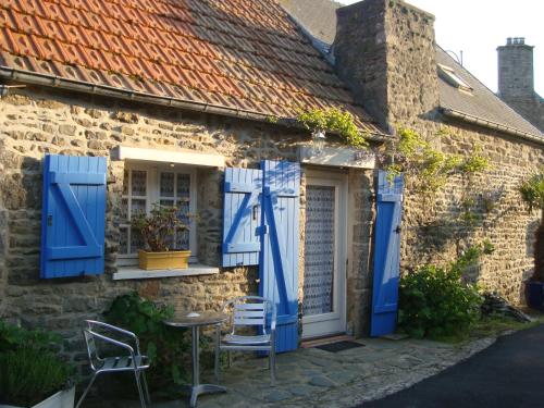 SurtainvilleにあるGîtes Rose des Sablesの青いシャッターとテーブルと椅子が備わる古い石造りの家