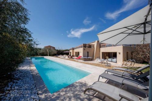 une piscine avec des chaises et un parasol à côté d'une maison dans l'établissement Villa Sérénité, à La Roque-sur-Pernes