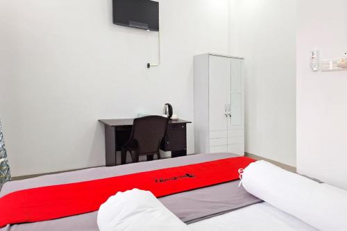 a bedroom with a red blanket on a bed with a desk at RedDoorz at Imanuel Homestay Tomohon in Tomohon