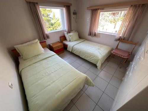 a bedroom with two beds and a chair and two windows at Villa Leonidas in Anavissos