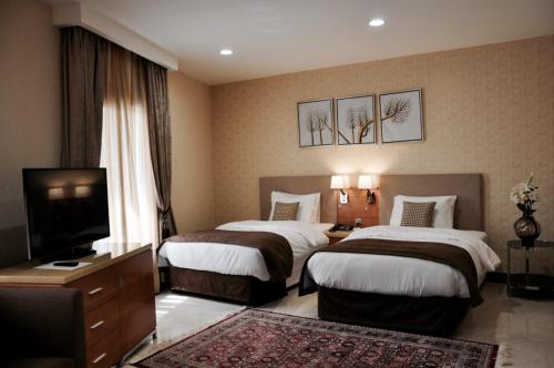Una habitación de hotel con dos camas y un televisor. en Asherij Hotel, en Doha