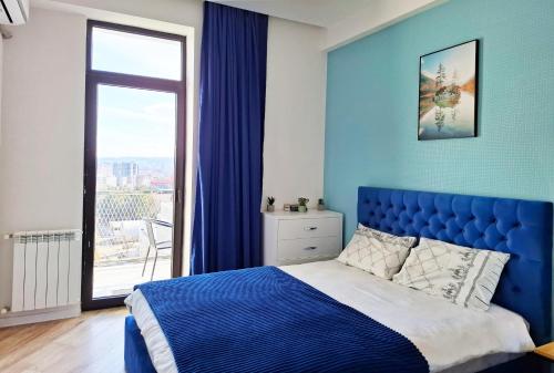 Dormitorio azul con cama y ventana grande en Cozy 1BR Apt near Metro Station on Saburtalo., en Tiflis