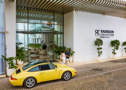 a man and woman standing next to a yellow car in front of a building at Radisson Collection Resort Galle in Galle