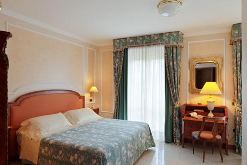 a bedroom with a bed and a desk and a mirror at Grand Hotel Bristol in Stresa