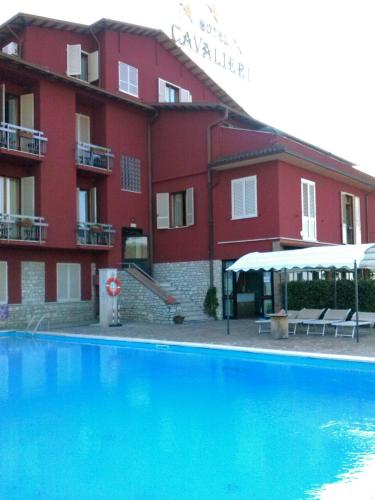a red building with a swimming pool in front of a building at Hotel Cavalieri in Passignano sul Trasimeno