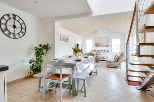 une salle à manger avec une table, des chaises et une horloge dans l'établissement Maison moderne à 80m de la plage - 6 personnes, à La Guérinière