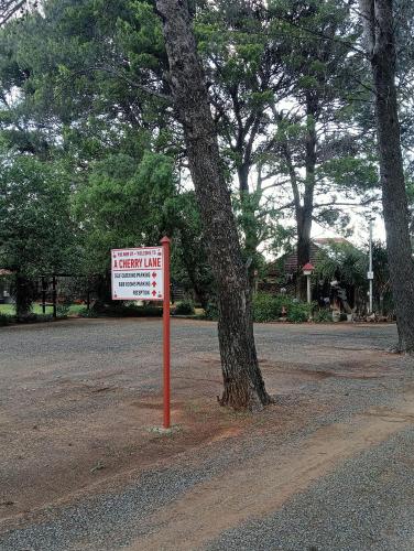 a sign sitting next to a tree in a park at A Cherry Lane Self Catering and B&B in Bloemfontein