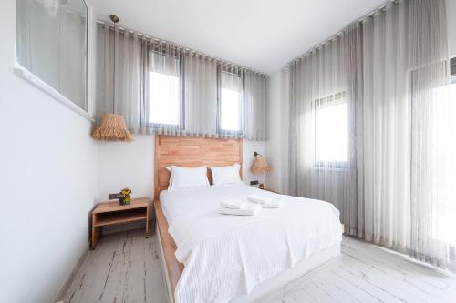 a bedroom with a bed with white sheets and windows at Dione Bozcaada in Bozcaada