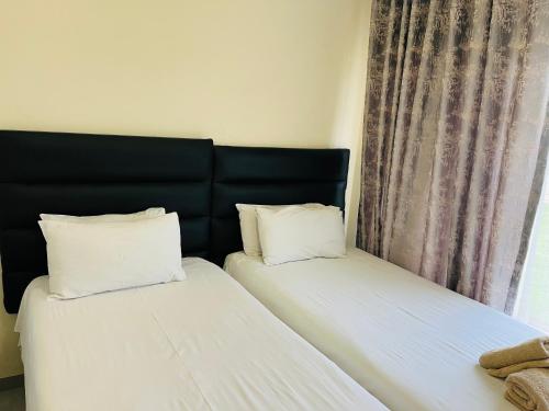 two beds with white pillows sitting next to a window at House 210 holiday rentals in Alberton