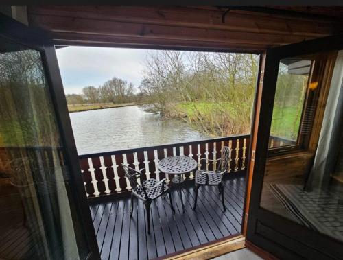 a balcony with a table and chairs and a view of a river at Bure River Lodge Houseboat in Stalham