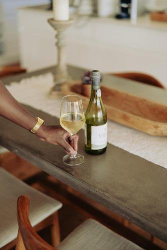 a person holding a glass of wine next to a bottle at Thyme & Tide Beach Villa in Yzerfontein