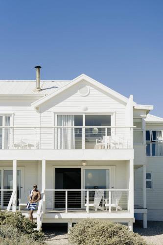 a man sitting on the front porch of a white house at Thyme & Tide Beach Villa in Yzerfontein