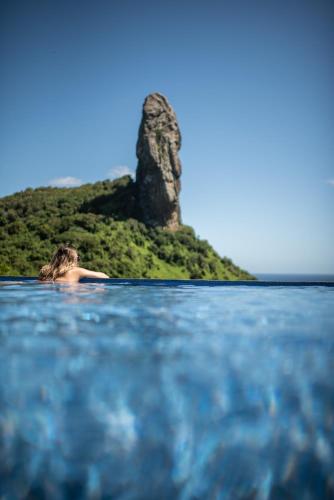 a woman laying in the water in front of an island at Pousada Morena in Fernando de Noronha