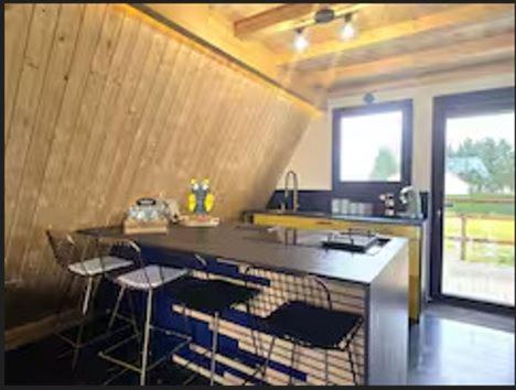 une cuisine avec un comptoir avec des tabourets et un évier dans l'établissement le chalet d'hibs, à Montreuil-le-Chétif