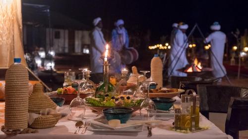 a table with food on it with people in the background at Merzouga Glossy Camp in Merzouga